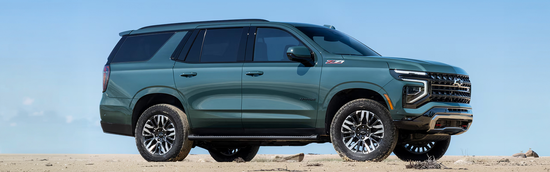 Teal 2026 Chevrolet Tahoe parked on a sandy terrain with a clear blue sky in the background.