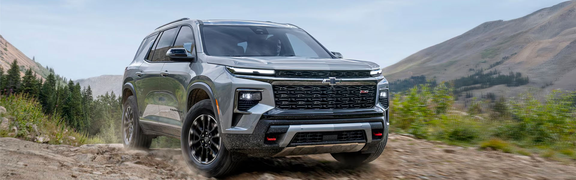 2026 Chevrolet Traverse navigating a dirt road with mountains in the background.